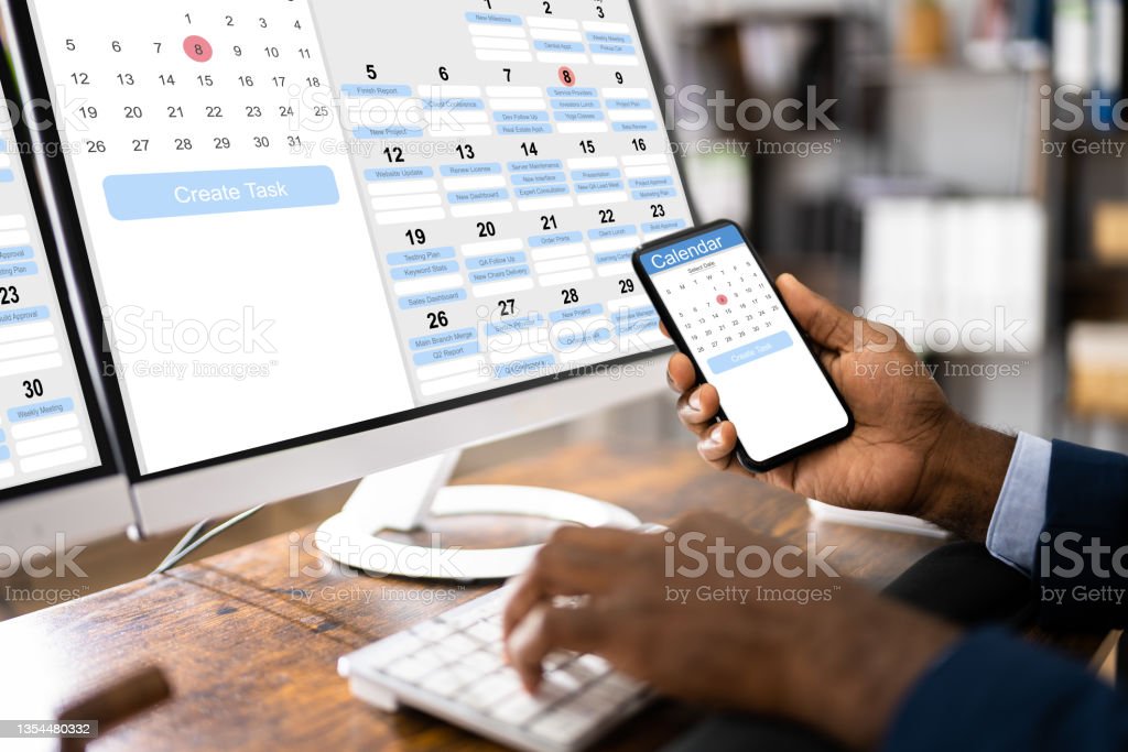 A person looking at an online calendar on a desktop and a phone. 