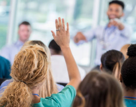 In a classroom of students, an instructor is calling on a woman raising her hand.