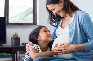 "pregnant woman and daughter hold her belly and smile at each other"