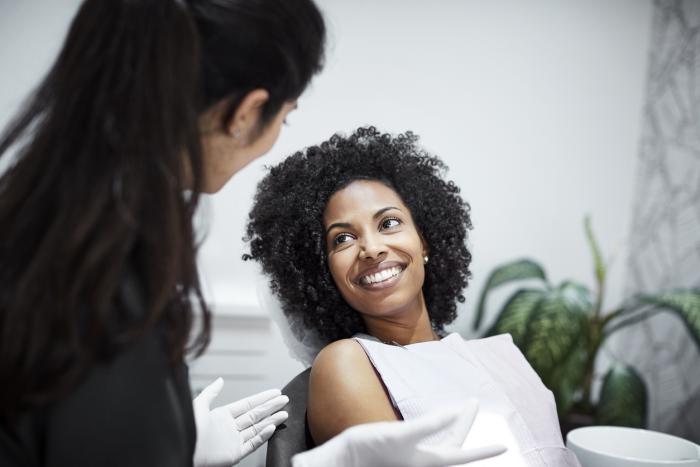 Woman with brown hair wearing a white dentist napkin smiling at a dentist with white gloves