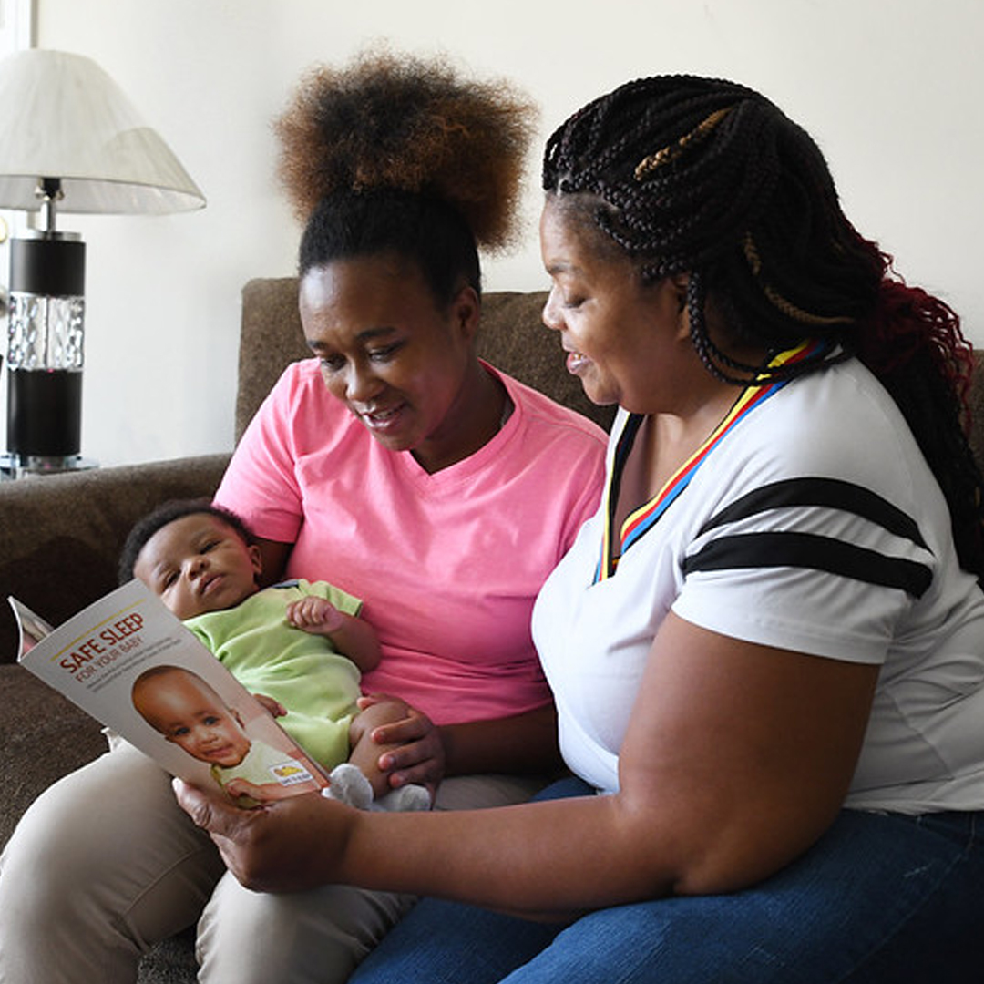 Two women reading a book on Sudden Infant Death Syndrome. One woman is holding an infant.