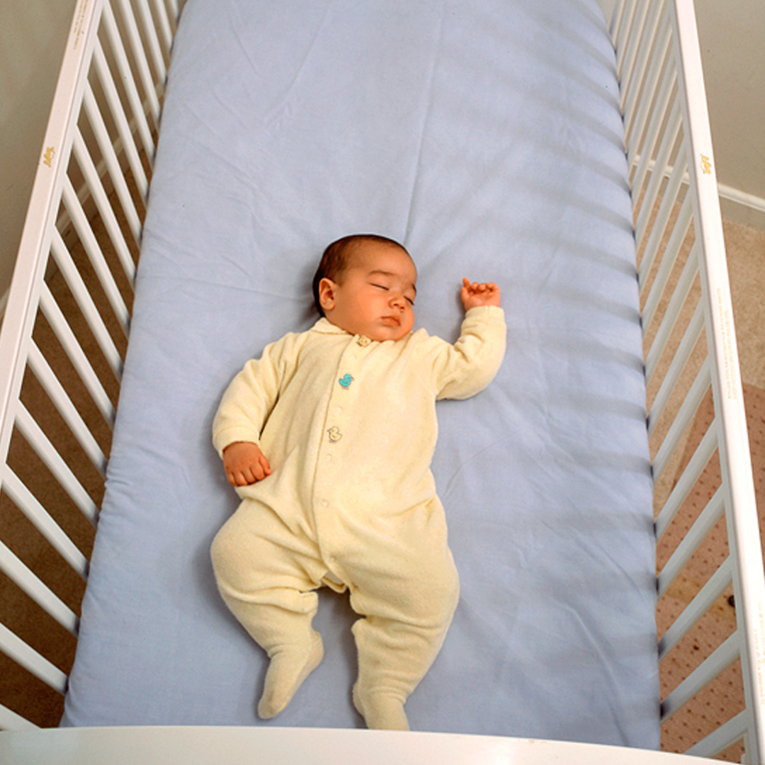 An infant laying on their back asleep in a crib.