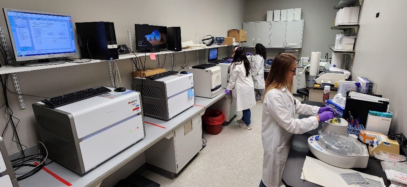 Three people wearing labcoats working on various instruments for PCR.