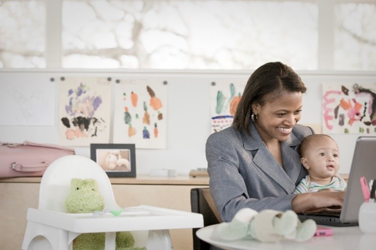 A mother typing at a computer with her baby.