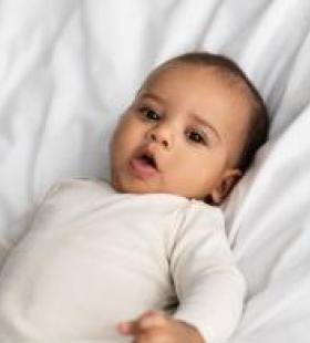 Baby laying on white sheets while coughing
