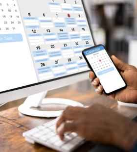 A person looking at an online calendar on a phone and a desktop computer.