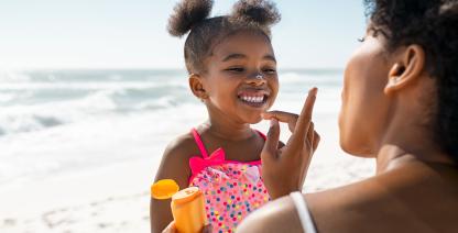 Una madre le pone protector solar a su pequeña hija en la playa.