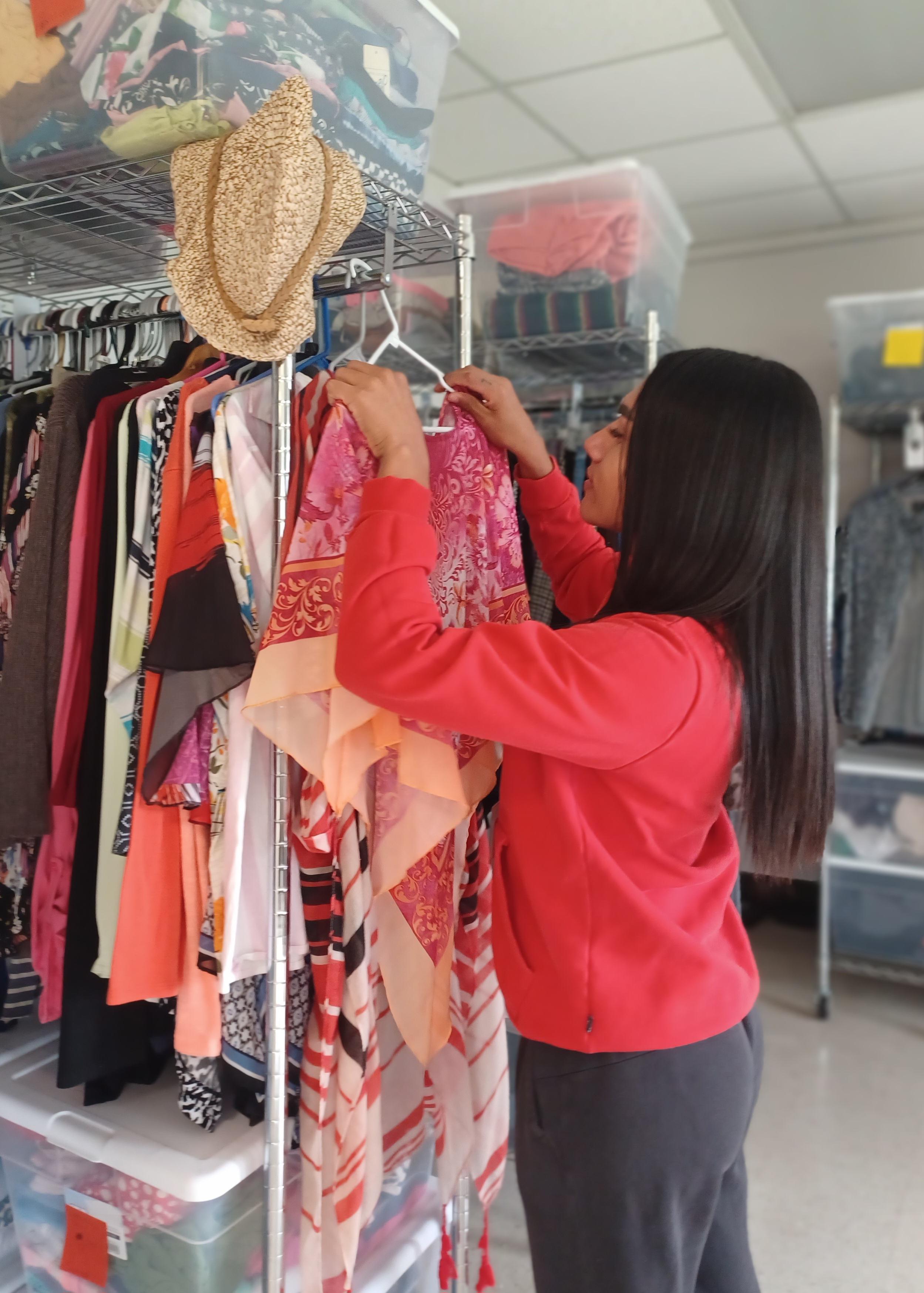 Person in a red top arranging clothing on a rack filled with colorful garments.