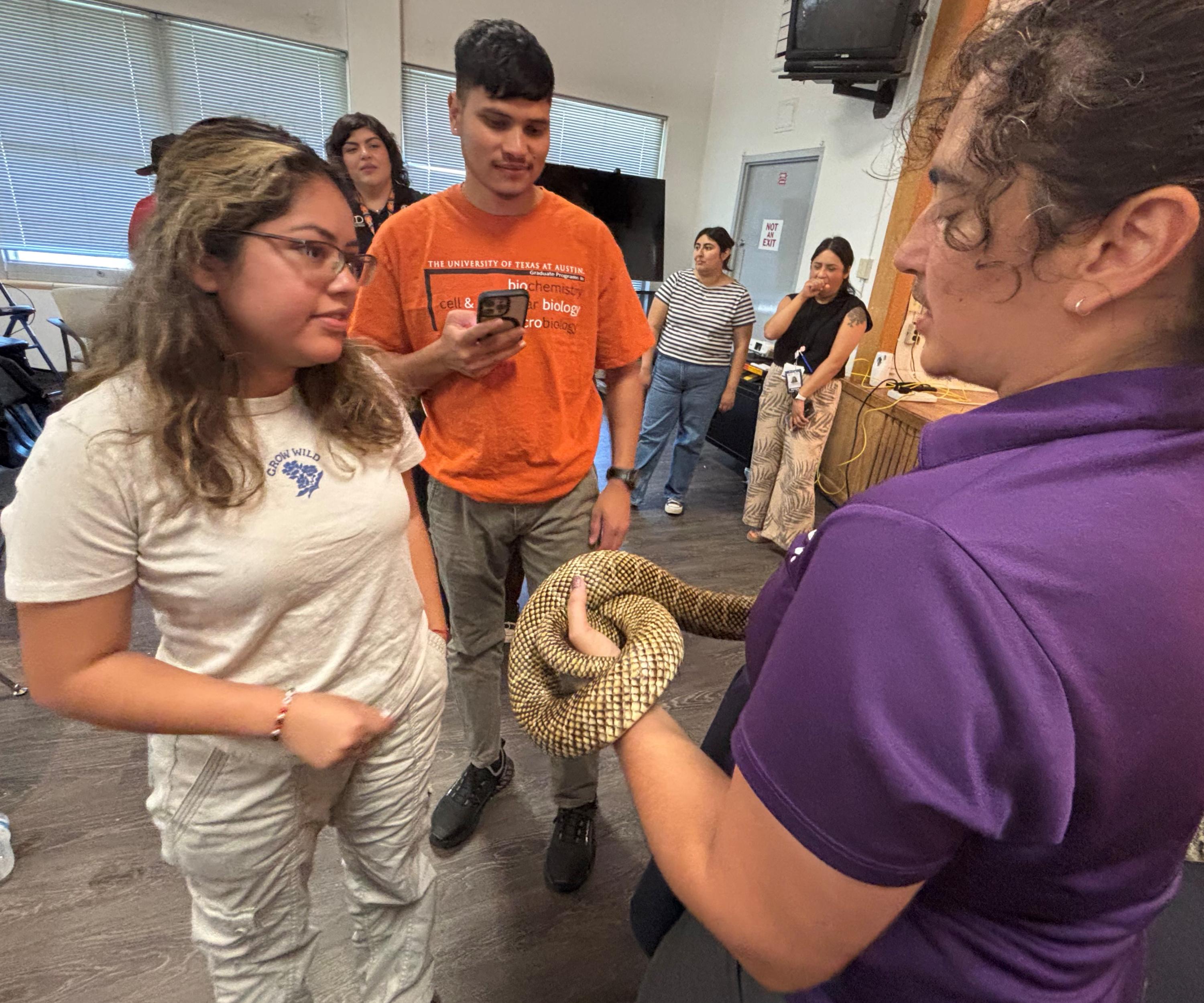 People gathered indoors, observing a person holding a snake.