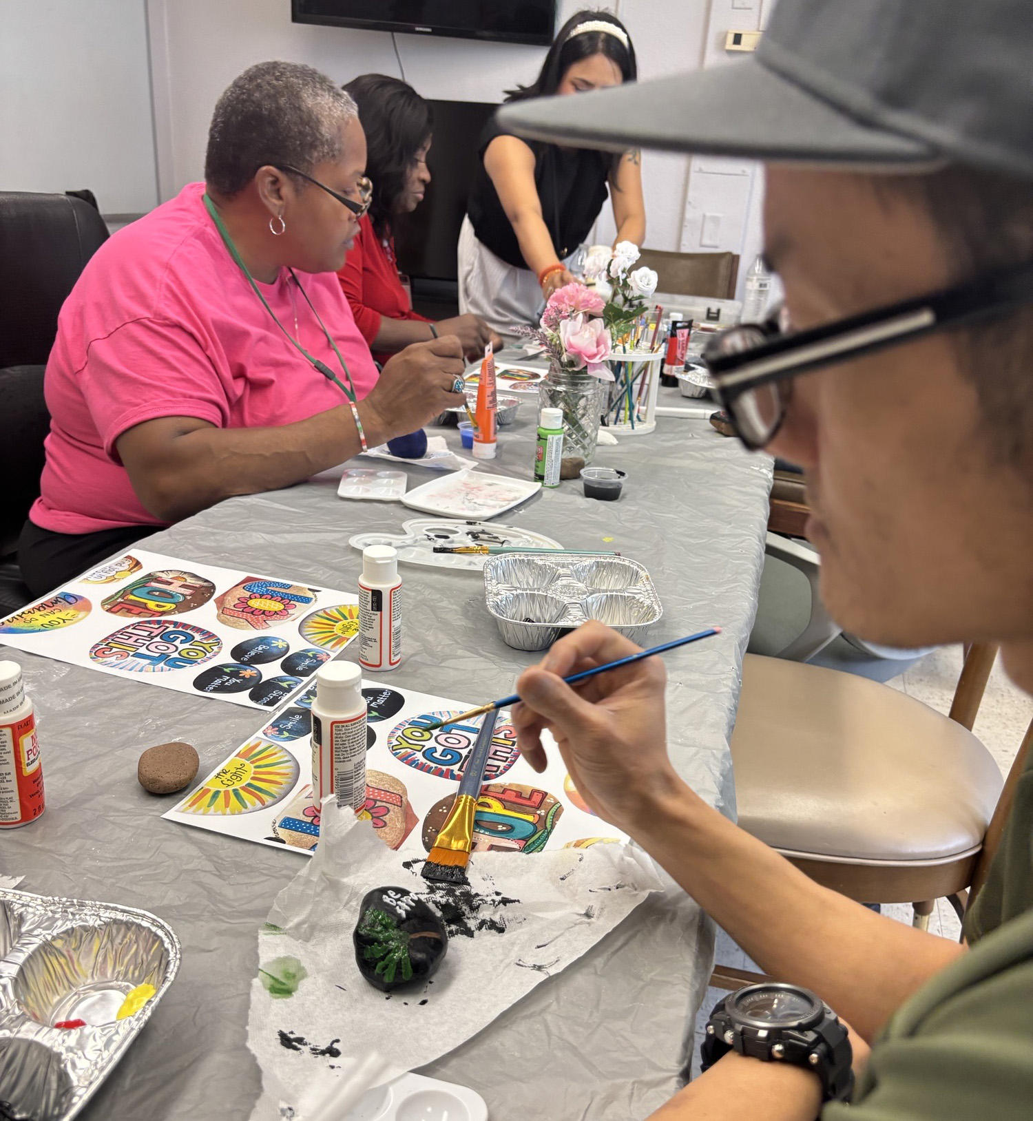 Personas pintando y haciendo manualidades en una mesa cubierta de materiales artísticos y decoraciones.