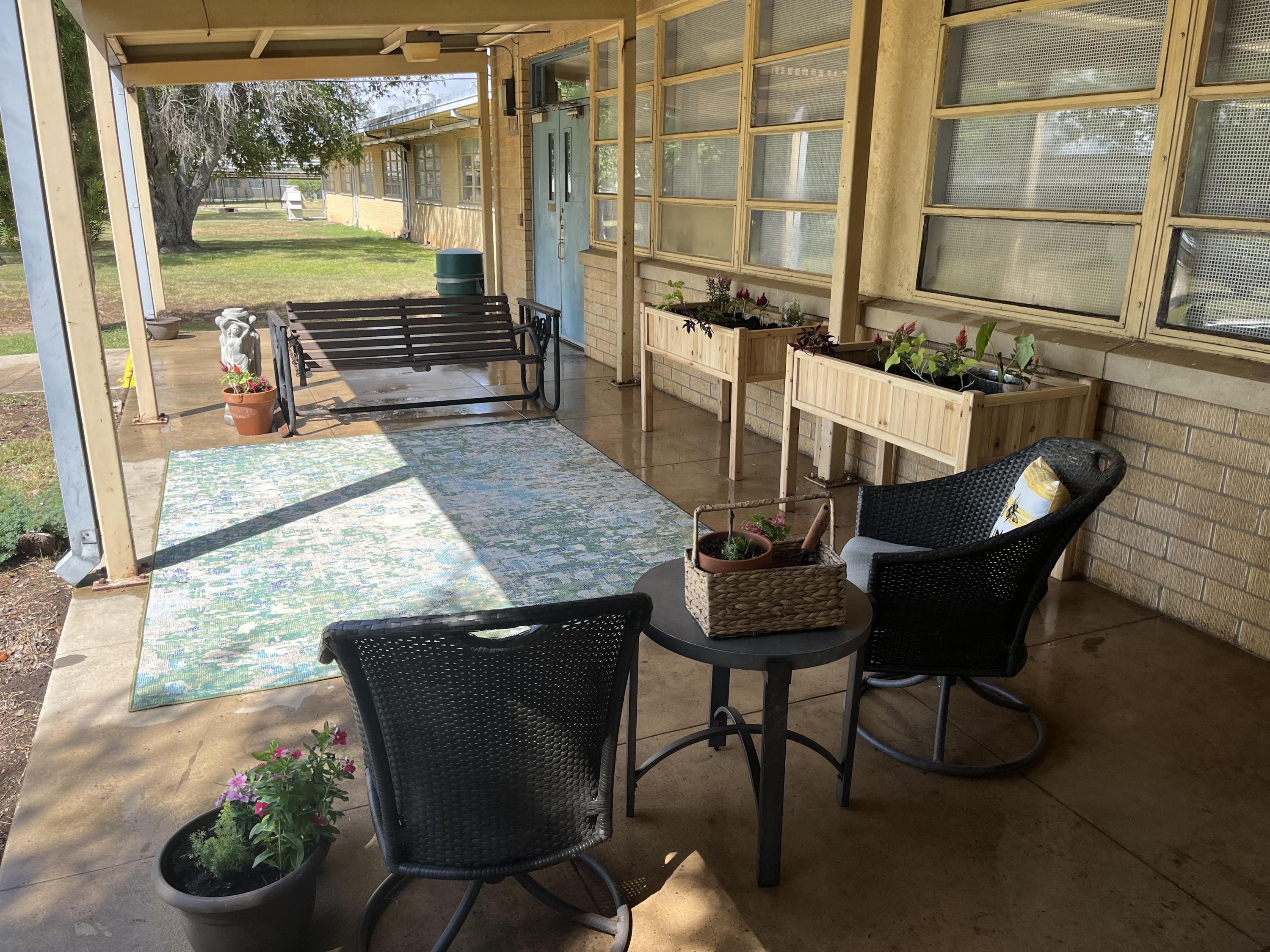 Un patio con sillas de mimbre, una mesa con plantas, una alfombra, un columpio y jardineras.