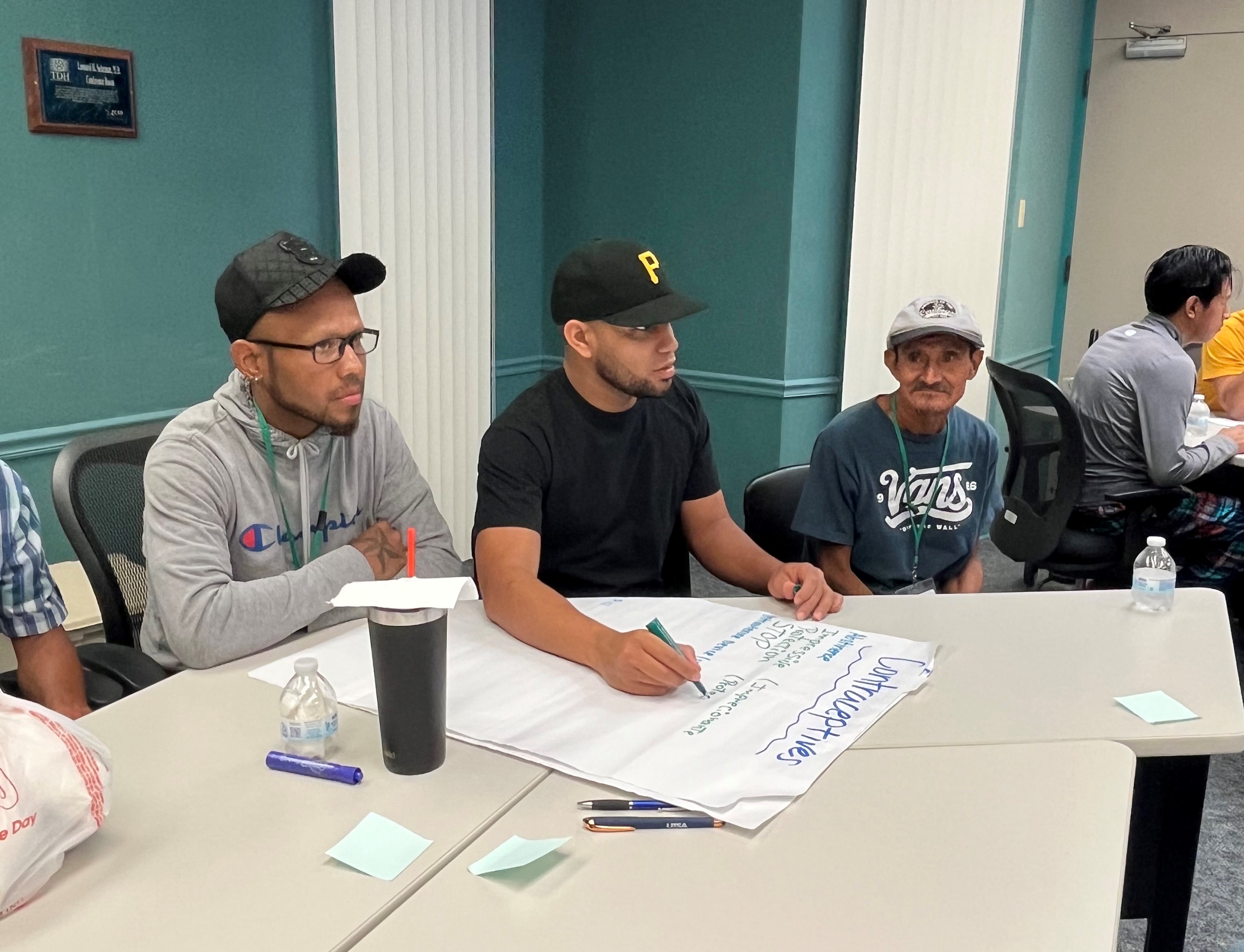 Four people seated at a table with papers and markers, engaged in a discussion.