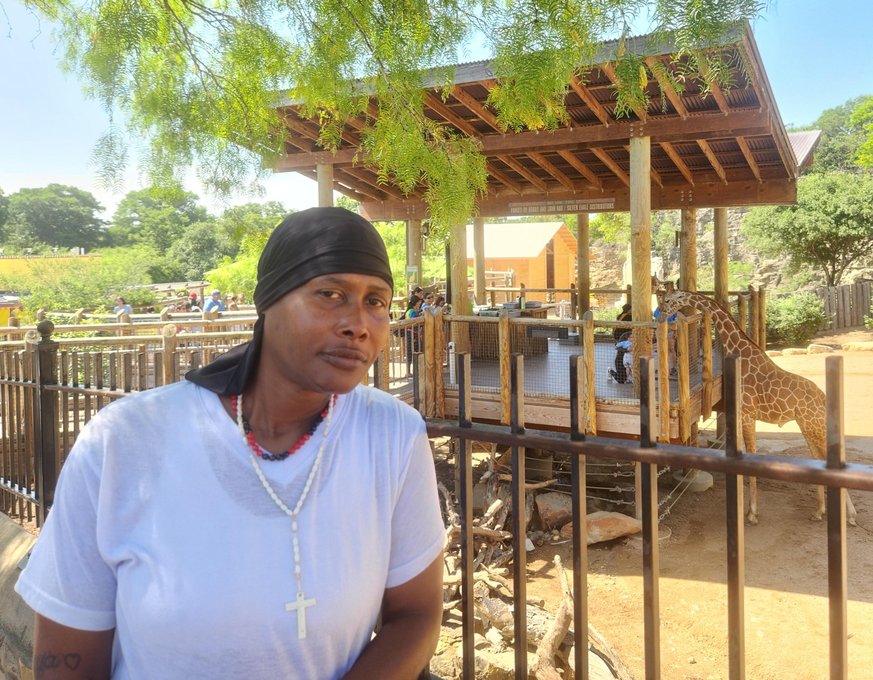 A woman poses before a giraffe at the zoo