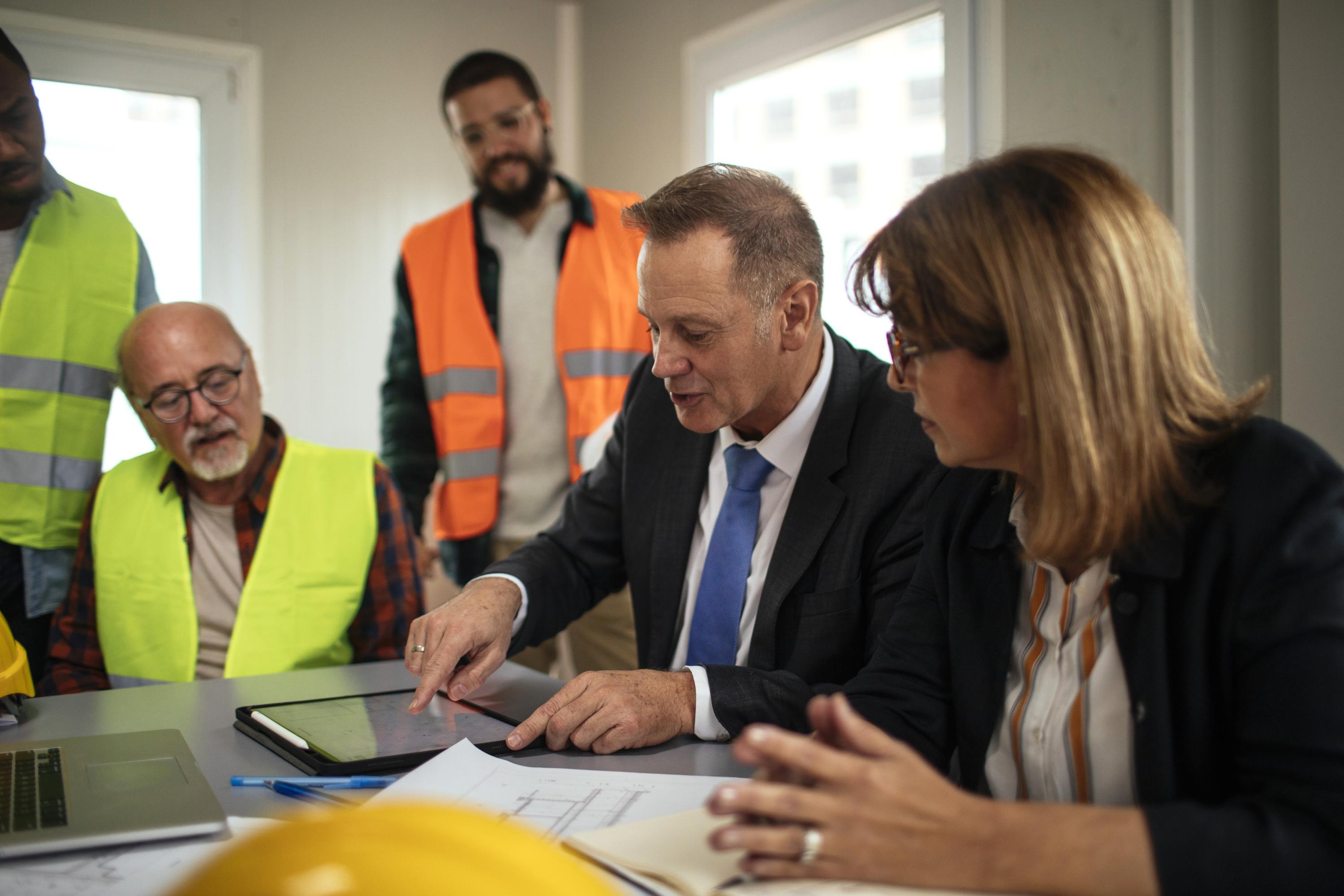 Work meeting in room with man pointing to a tablet.
