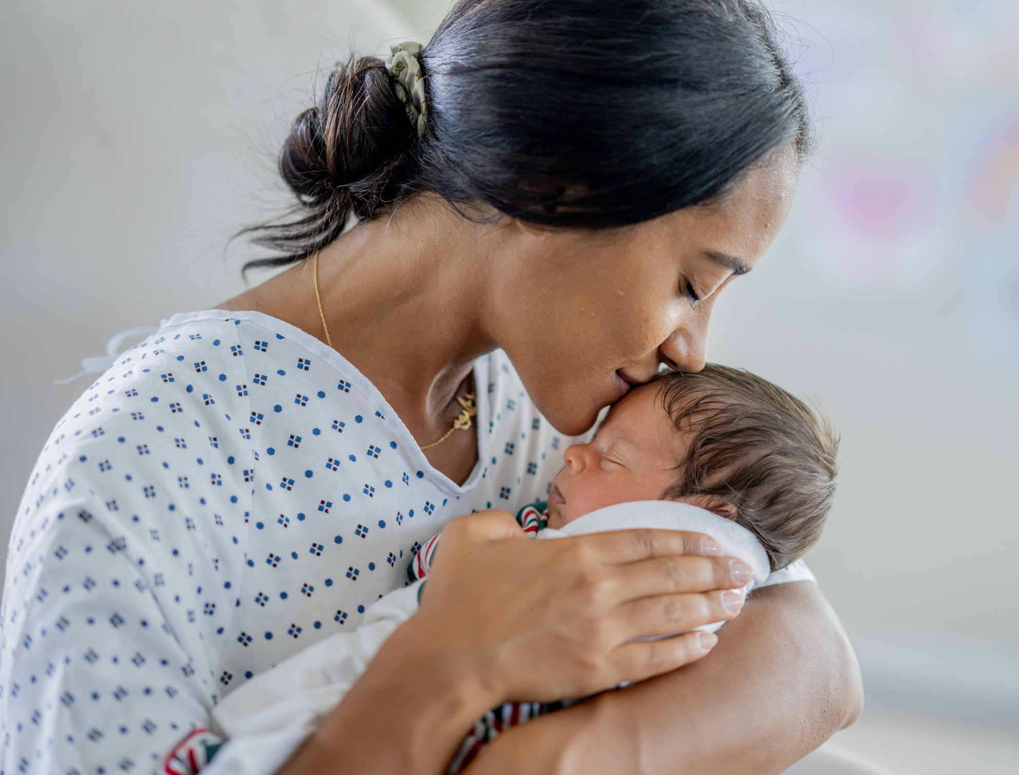 Mother holding and kissing newborn on the forehead