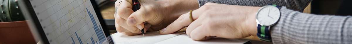 A woman takes notes while looking at a laptop.