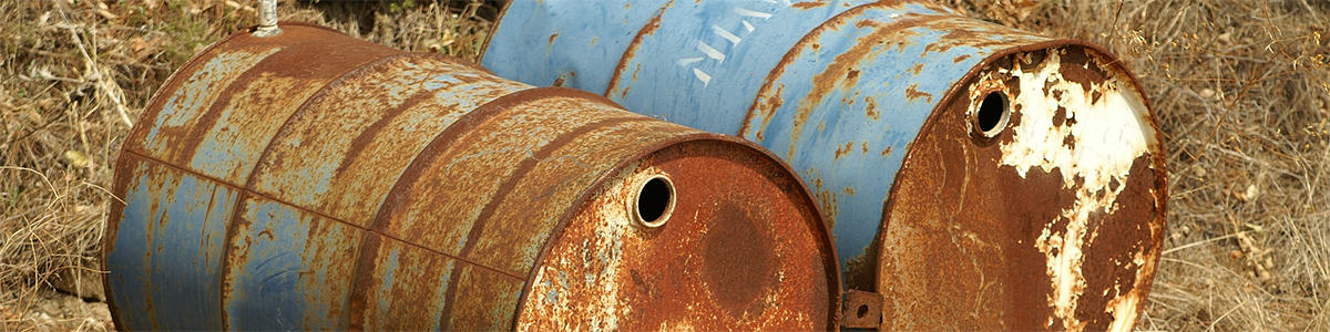 Two rusty old barrels laying in a filed.