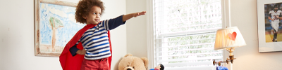 A young child in his bedroom pretends he is a superhero