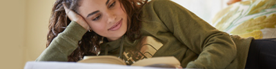 A teen girl lies down reading a book.
